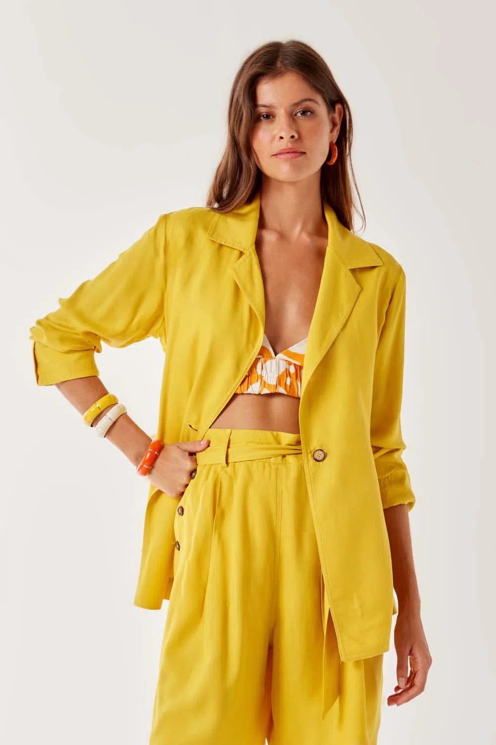 mulher usando um conjunto de alfaiataria blazer e calça amarelos e um cropped estampado